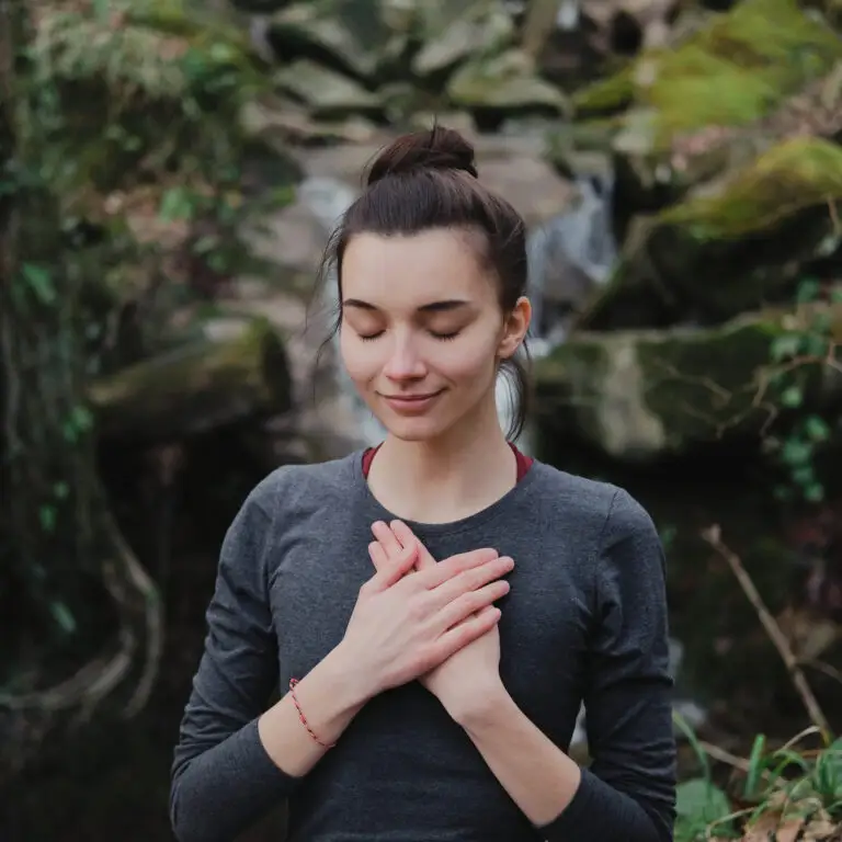 Young woman practicing breathing yoga pranayama outdoors in moss forest on background of waterfall. Unity with nature concept.