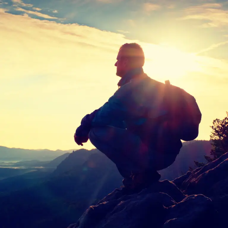 Hiker with sporty backpack sit on rocky cliff edge